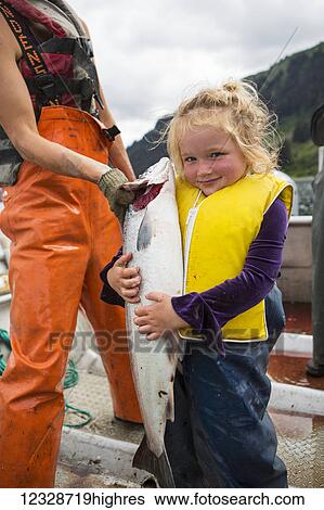 Stock Photograph - Young girl holding a large red salmon while standing in a set-net skiff, South-central Alaska; Seldovia, Alaska, United States of America. Fotosearch