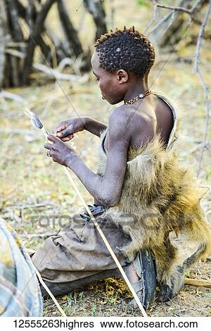 Young Hadzabe hunter wearing baboon skin cloak fletches arrow with feathers from a bird shot earlier in the morning near Lake Eyasi; Tanzania View Large Photo Image Stock Photograph - Young Hadzabe hunter wearing baboon skin cloak fletches arrow with feathers from a bird shot earlier in the morning near Lake Eyasi; Tanzania. Fotosearch