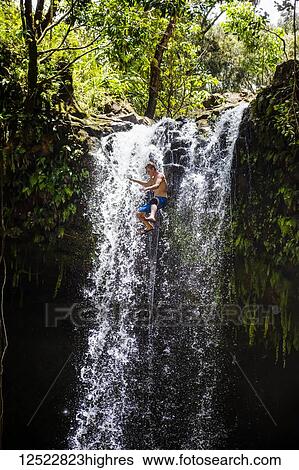 Young man jumps from a waterfall; Hana, Maui, Hawaii, United States of America View Large Photo Image Stock Photograph - Young man jumps from a waterfall; Hana, Maui, Hawaii, United States of America. Fotosearch