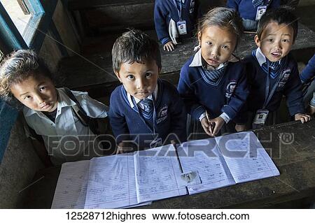 Stock Photograph - Young students wearing uniforms standing in a classroom and looking up at the camera; Sikkim, India. Fotosearch