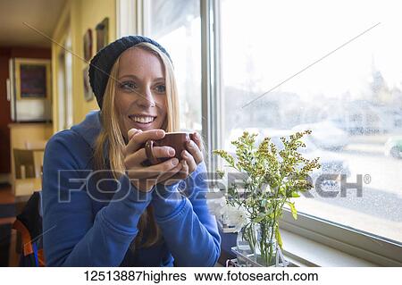 Stock Photograph - Young woman enjoying a hot beverage in a cafe in downtown Anchorage, South-central Alaska; Anchorage, Alaska, United States of America. Fotosearch