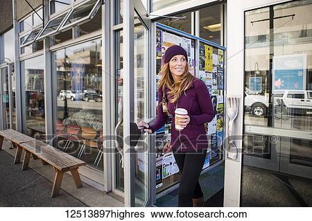 Stock Photograph - Young woman leaving a cafe with a drink in downtown Anchorage, South-central Alaska; Anchorage, Alaska, United States of America. Fotosearch