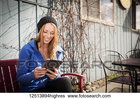 Stock Photograph - Young woman sitting with her tablet outside a business in downtown Anchorage, South-central Alaska; Anchorage, Alaska, United States of America. Fotosearch