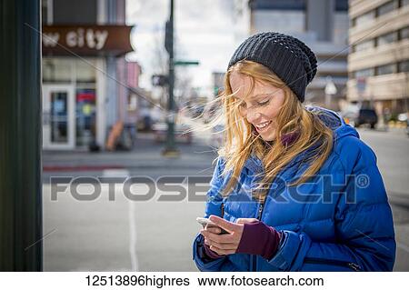 Stock Photograph - Young woman texting on her smartphone in downtown Anchorage, South-central Alaska; Anchorage, Alaska, United States of America. Fotosearch