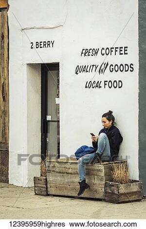Young woman using her smart phone outside a coffee shop in Williamsburg; Brooklyn, New York, United States of America View Large Photo Image Stock Photograph - Young woman using her smart phone outside a coffee shop in Williamsburg; Brooklyn, New York, United States of America. Fotosearch
