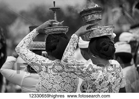 Stock Photograph - Young Women At A Religious Ceremony Carrying A Smoking Offering On Her Head; Bali, Indonesia. Fotosearch