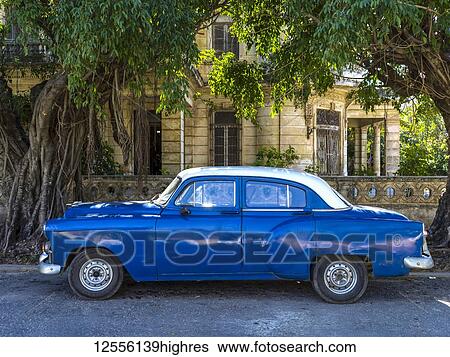 Stock Photograph - Blue vintage car parked on the street outside a house; Havana, Cuba. Fotosearch