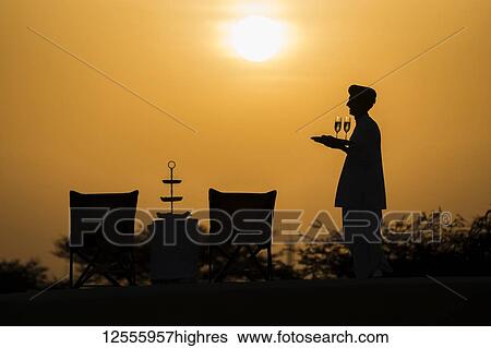 Butler holding champagne glasses after setting up a table for a sundowner drink; Rajasthan, India View Large Photo Image Stock Photograph - Butler holding champagne glasses after setting up a table for a sundowner drink; Rajasthan, India. Fotosearch