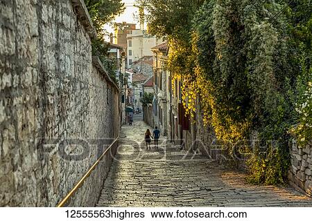 Stock Photograph - Couple walking down a narrow street holding hands; Pula, Istria, Croatia. Fotosearch