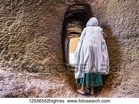 Stock Photograph - Ethiopian woman entering rock-cut tunnel between Biete Medhane Alem (House of the Saviour of the World) and Biete Mariam (House of Mary) Ethiopian Orthodox underground monolith rock-cut churches in the Northern Group of the Rock-Hewn Churches;.... Fotosearch