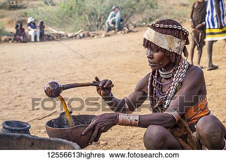 Stock Photograph - Hamer woman preparing a ceremonial drink at a bull jumping ceremony, which initiates a boy into manhood, in the village of Asile, Omo Valley; Southern Nations Nationalities and Peoples' Region, Ethiopia. Fotosearch