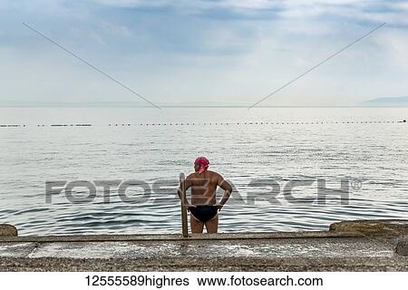 Stock Photograph - Male swimmer stands looking out at the coastline and the Adriatic Sea; Opatija, Primorje-Gorski Kotar County, Croatia. Fotosearch