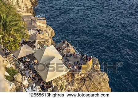 Stock Photograph - People enjoying the sunset in a bar on a cliff outside the City Walls; Dubrovnik, Dubrovnik-Neretva County, Croatia. Fotosearch