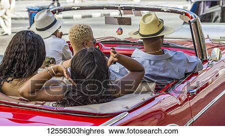 Stock Photograph - Three woman and two men ride in a red convertible car; Havana, Cuba. Fotosearch
