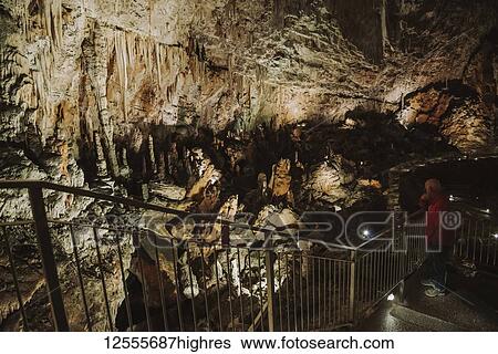 Stock Photograph - Tourists on steps and exploring in an underground cave with rock walls illuminated with light; Italy. Fotosearch