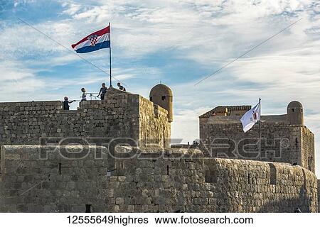 Stock Photograph - Tourists on the walls of a historic fortication with flag; Dubrovnik, Dubrovnik-Neretva County, Croatia. Fotosearch