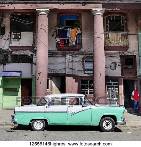 Stock Photograph - Vintage car parked in front of residential building; Havana, Cuba. Fotosearch