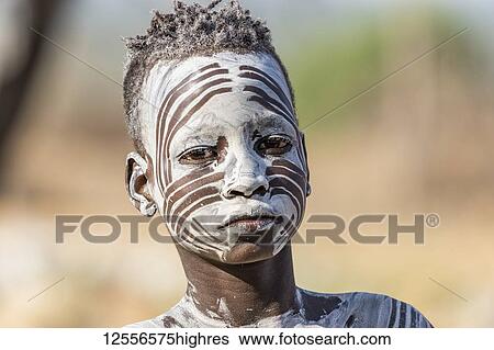 Stock Photograph - Young Karo man getting his face decorated with traditional face paint at Kortcho Village; Omo Valley, Ethiopia. Fotosearch