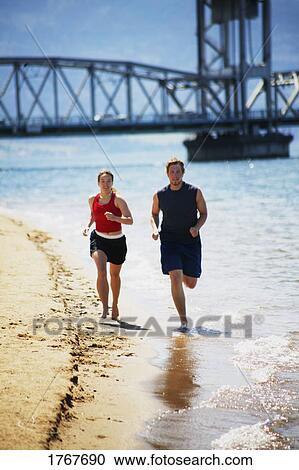 Stock Image - Couple jog together along the shore. Fotosearch