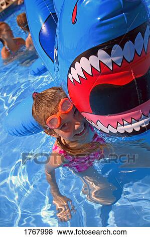 Stock Photo - Girl playing in swimming pool with inflatable shark. Fotosearch