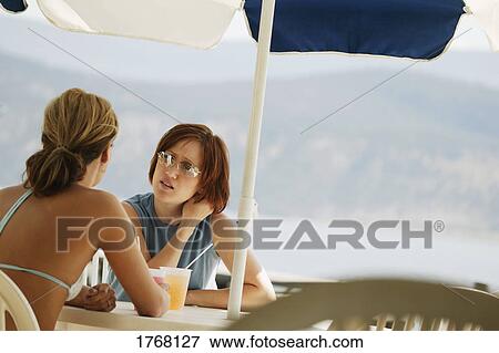 Two women in conversation at a beach cafe View Large Photo Image Stock Photo - Two women in conversation at a beach cafe. Fotosearch