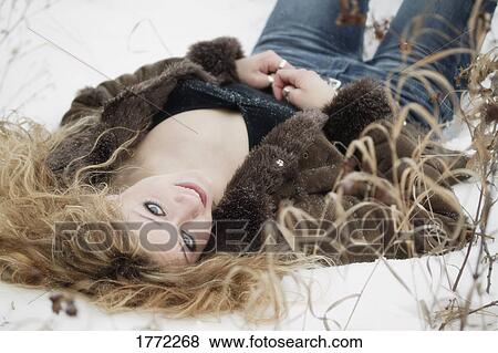 Stock Photo - Beautiful young woman laying on the snow. Fotosearch