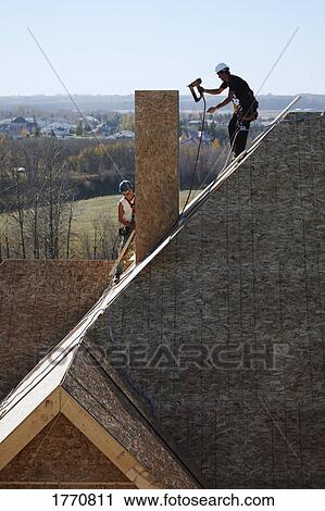 Stock Image - Construction worker on roof of house. Fotosearch