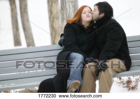 Stock Image - Couple on bench cuddling. Fotosearch
