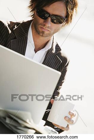 Stock Photograph - Man working on computer holding coffee. Fotosearch