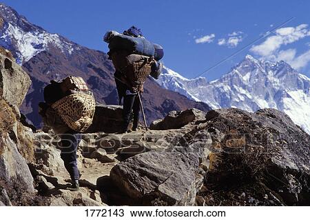 Stock Image - Men carrying heavy loads up mountain. Fotosearch