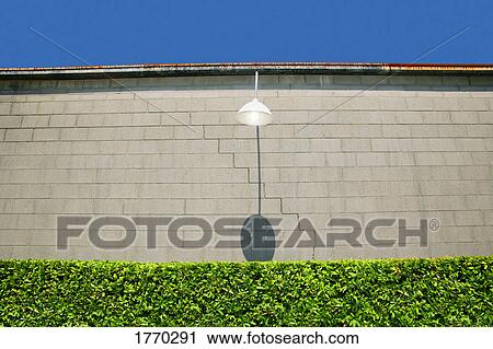 Stock Image - Street light against wall background and hedge. Fotosearch