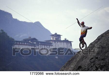 Stock Photograph - Unicyclist riding down hill with old building in background. Fotosearch