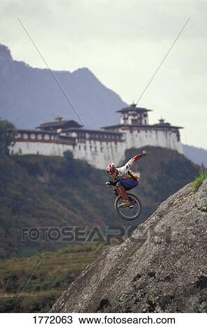 Stock Image - Unicyclist riding down hill with building in background. Fotosearch