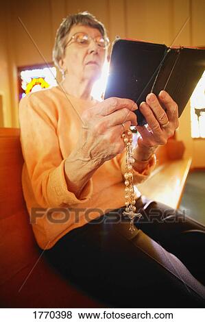 Stock Photo - Woman holding rosary beads and bible. Fotosearch