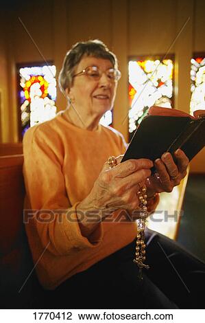 Stock Image - Woman reading bible & holding rosary beads. Fotosearch