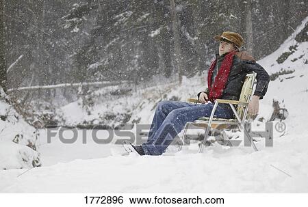 Stock Photograph - Man sitting on chair in snow. Fotosearch
