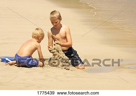 Stock Photo - Brothers building sandcastle on beach. Fotosearch