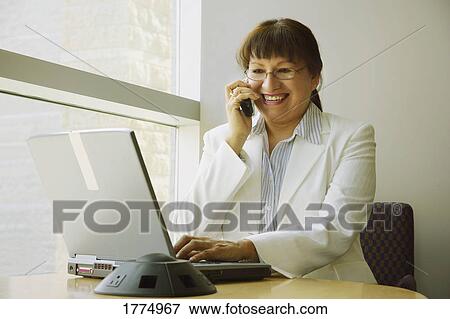Businesswoman talking on phone and working on laptop View Large Photo Image Stock Photo - Businesswoman talking on phone and working on laptop. Fotosearch