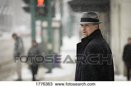 Stock Image - Man wearing a grey trilby and dark overcoat. Fotosearch