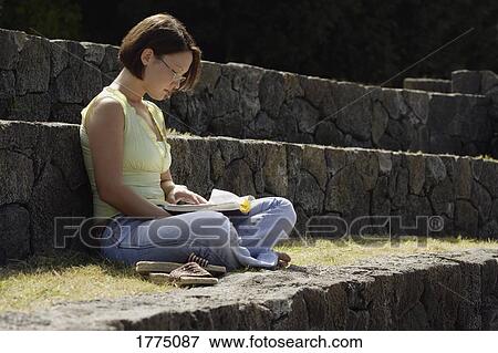 Student sitting on a stone seat reading a book View Large Photo Image Stock Photo - Student sitting on a stone seat reading a book. Fotosearch