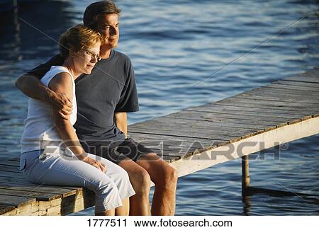 Stock Image - A couple sitting on a dock on the water. Fotosearch