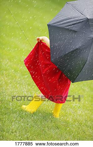 Stock Photography - A little girl walking in the rain while holding an umbrella.. Fotosearch