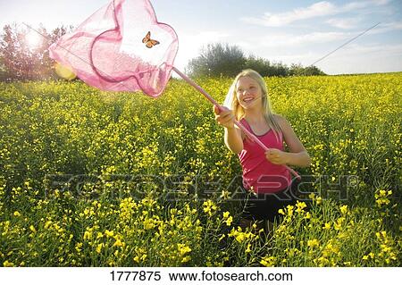 Stock Photography - A young lady catching a butterfly in a field of canola flowers. Fotosearch