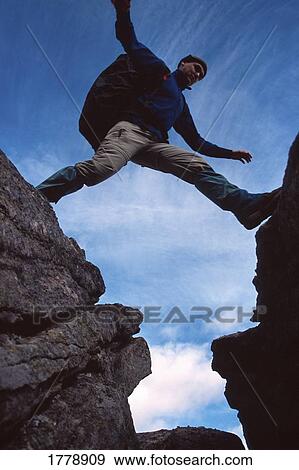 Stock Photo - Hiker jumps across a gap. Fotosearch