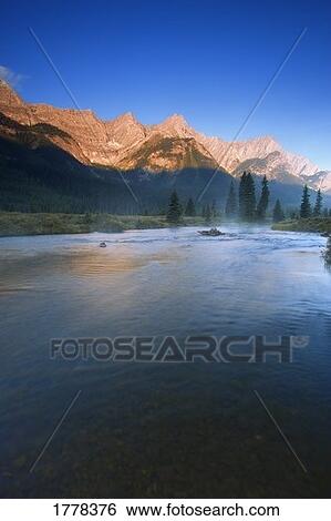Stock Photograph - Sunrise and early morning mist on river Elk Lakes. Fotosearch
