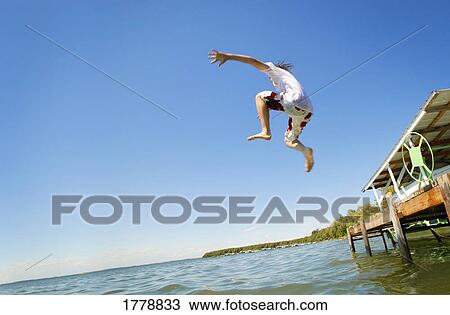 Teenager jumping off deck into water View Large Photo Image Stock Image - Teenager jumping off deck into water. Fotosearch