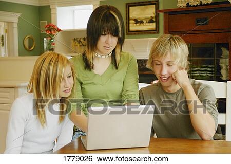 Stock Photograph - Teens gather around a laptop. Fotosearch