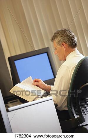 Picture - Man reading book in his office. Fotosearch