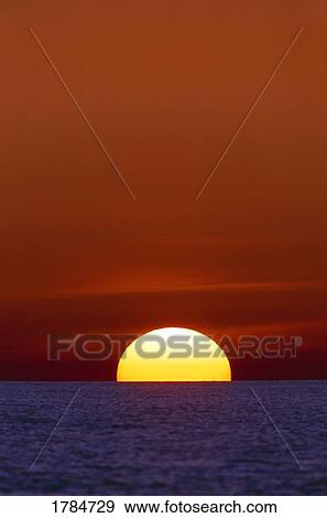 Stock Photo - Sun setting over the ocean. Fotosearch