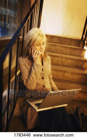 Stock Photograph - Woman talking on cell phone while working on lap top. Fotosearch